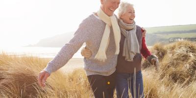 Senior Couple Walking Through Sand Dunes On Winter Beach Smiling